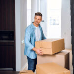 handsome man holding box in hands and smiling in new home